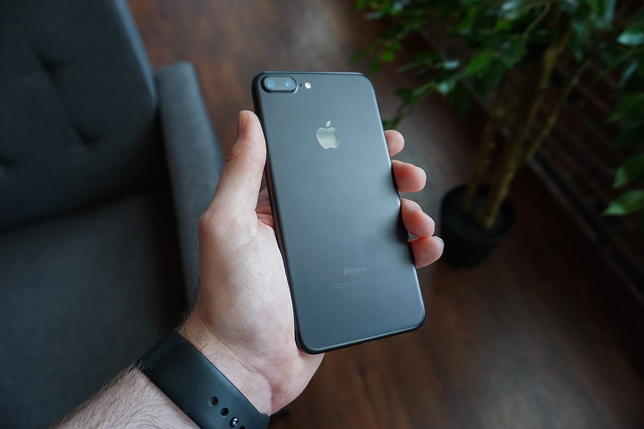 Mão segura um telefone celular preto ao ar livre.