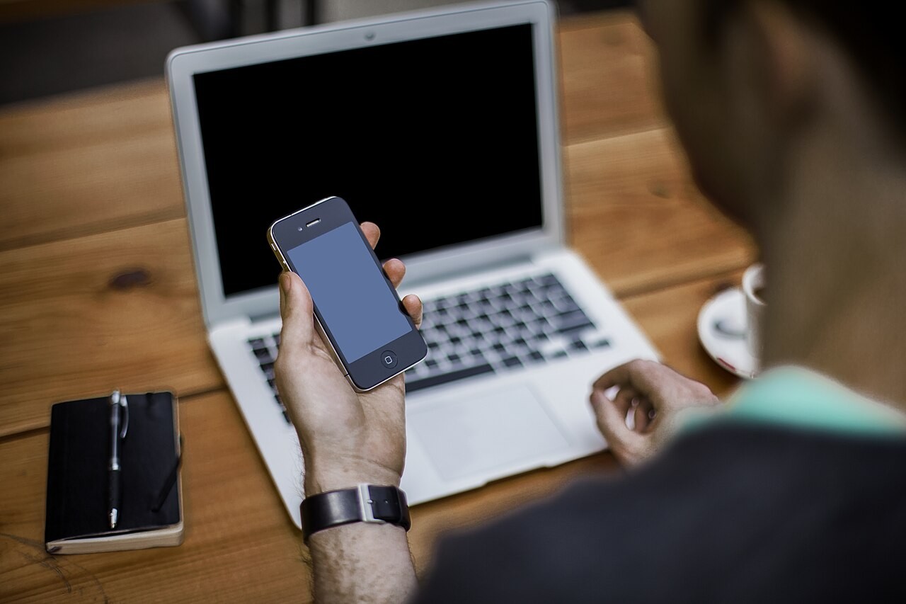 Pessoa utiliza celular ao lado de um notebook