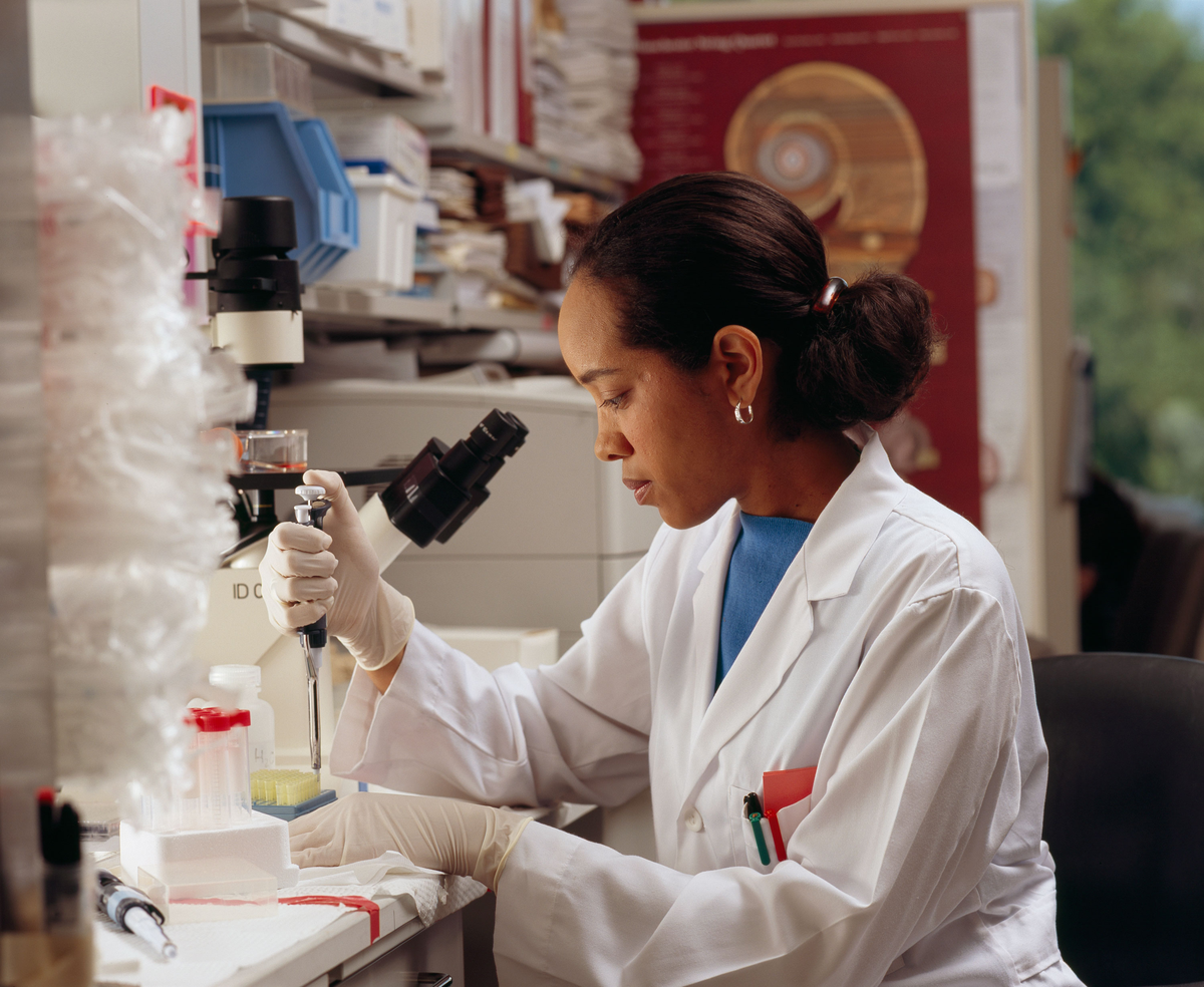 Pesquisadora com pipeta em bancada de laboratório.